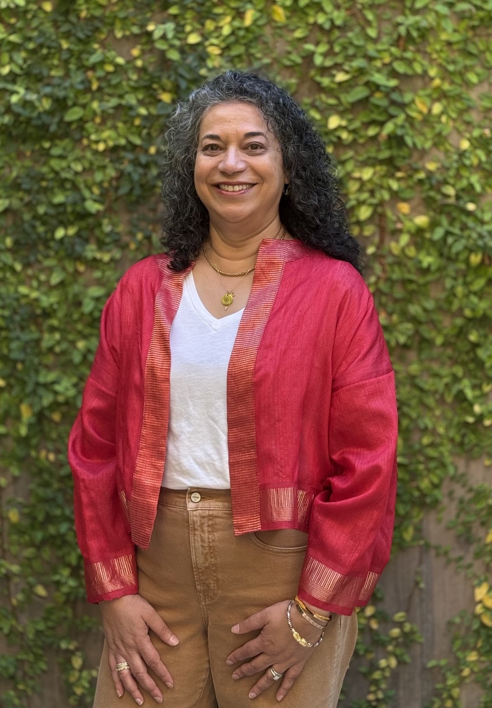 Chandre, founder of Chand Collective, wearing a red jacket in front of a leafy garden wall.