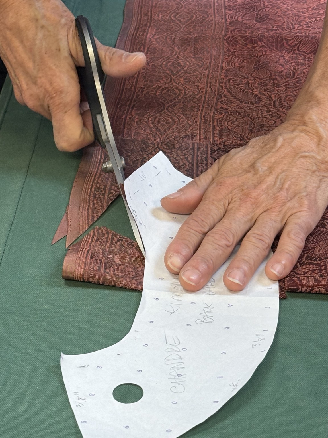 Hands cutting silk along a curved paper pattern
